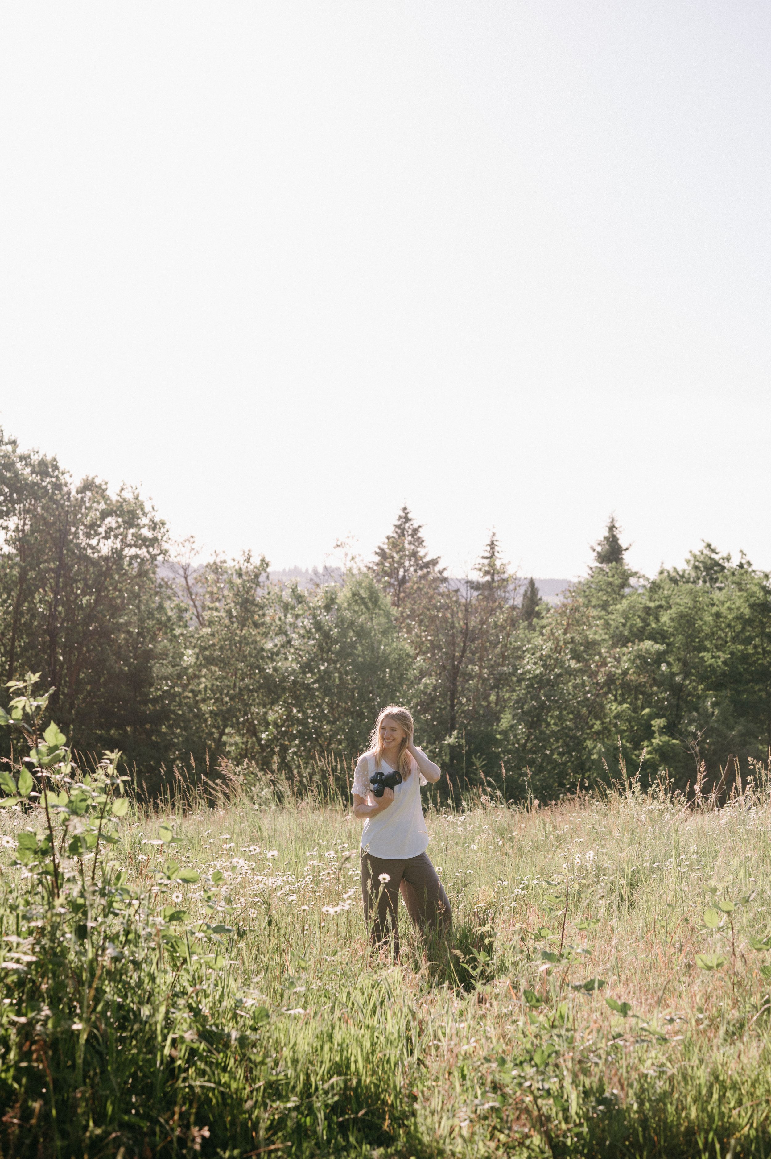Blonde woman in golden sunset light gently stroking a dark horse while holding reins in a fenced pasture.