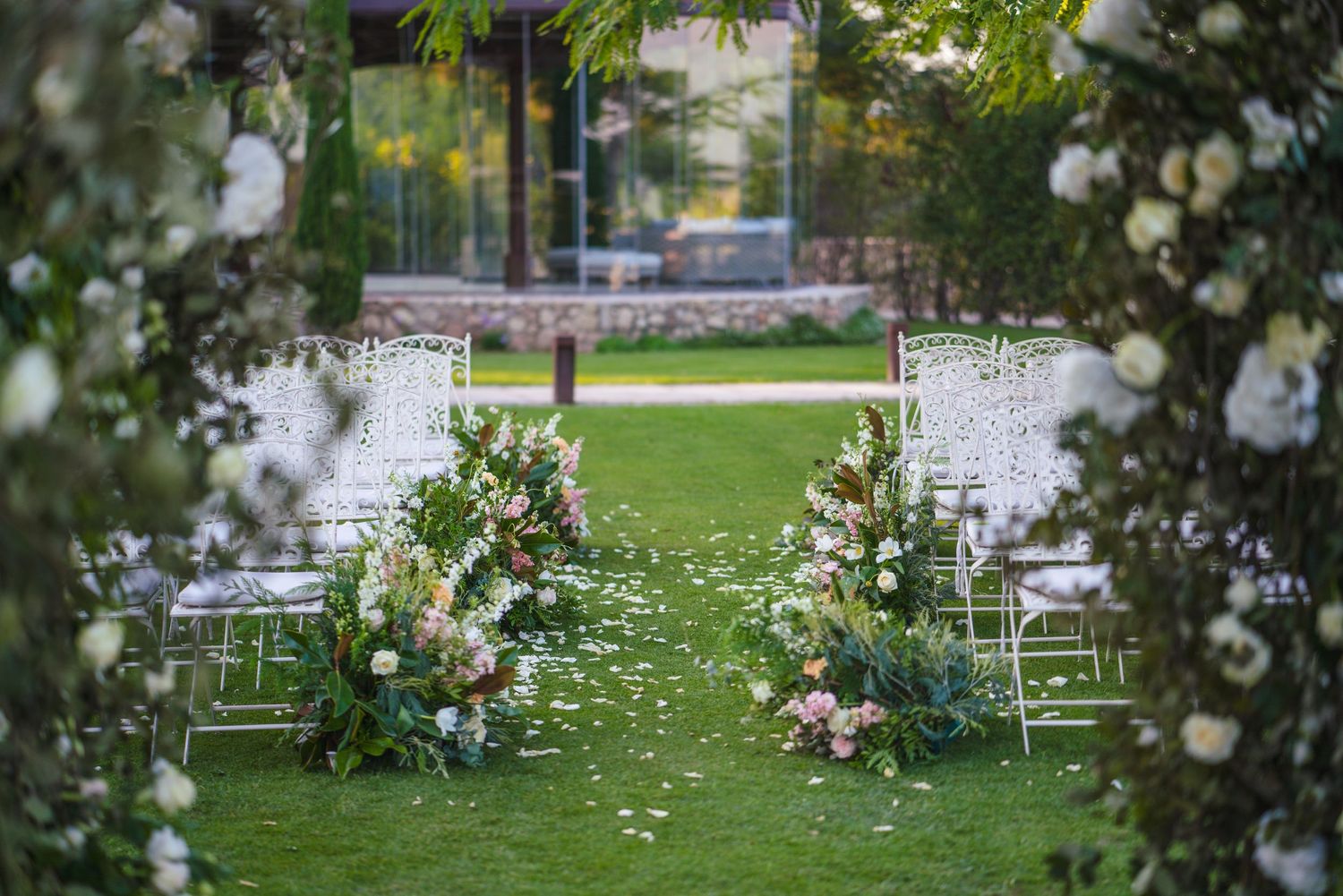 An outdoor wedding ceremony setup with white chairs and floral arrangements in a garden setting.