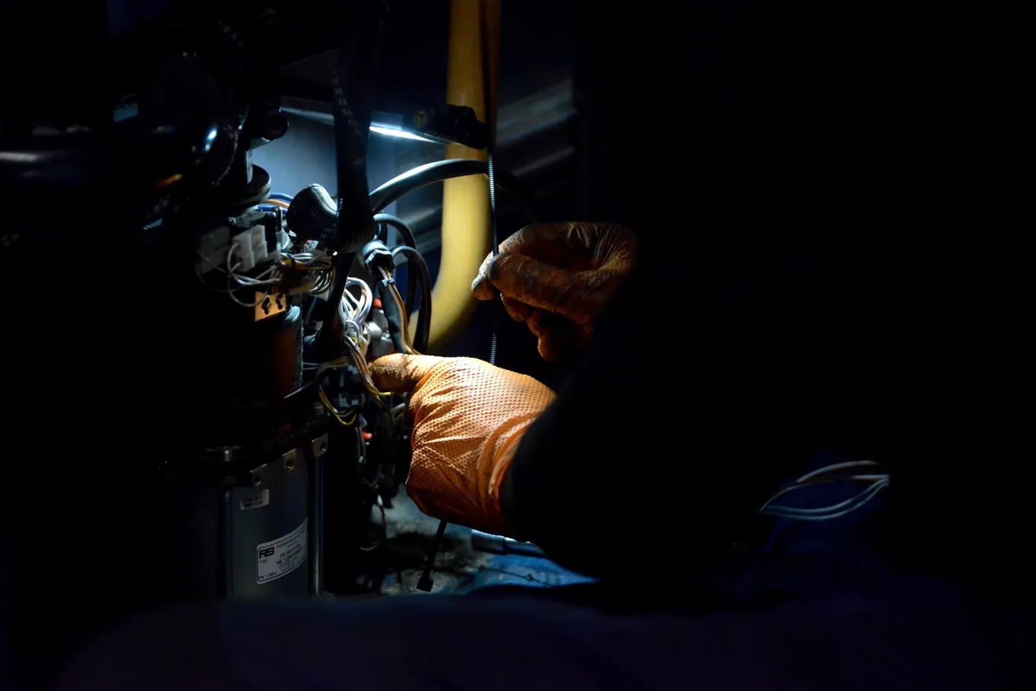 Plan sombre d’un technicien intervenant à l’intérieur du compartiment moteur d’un bus, vêtu de gants orange.