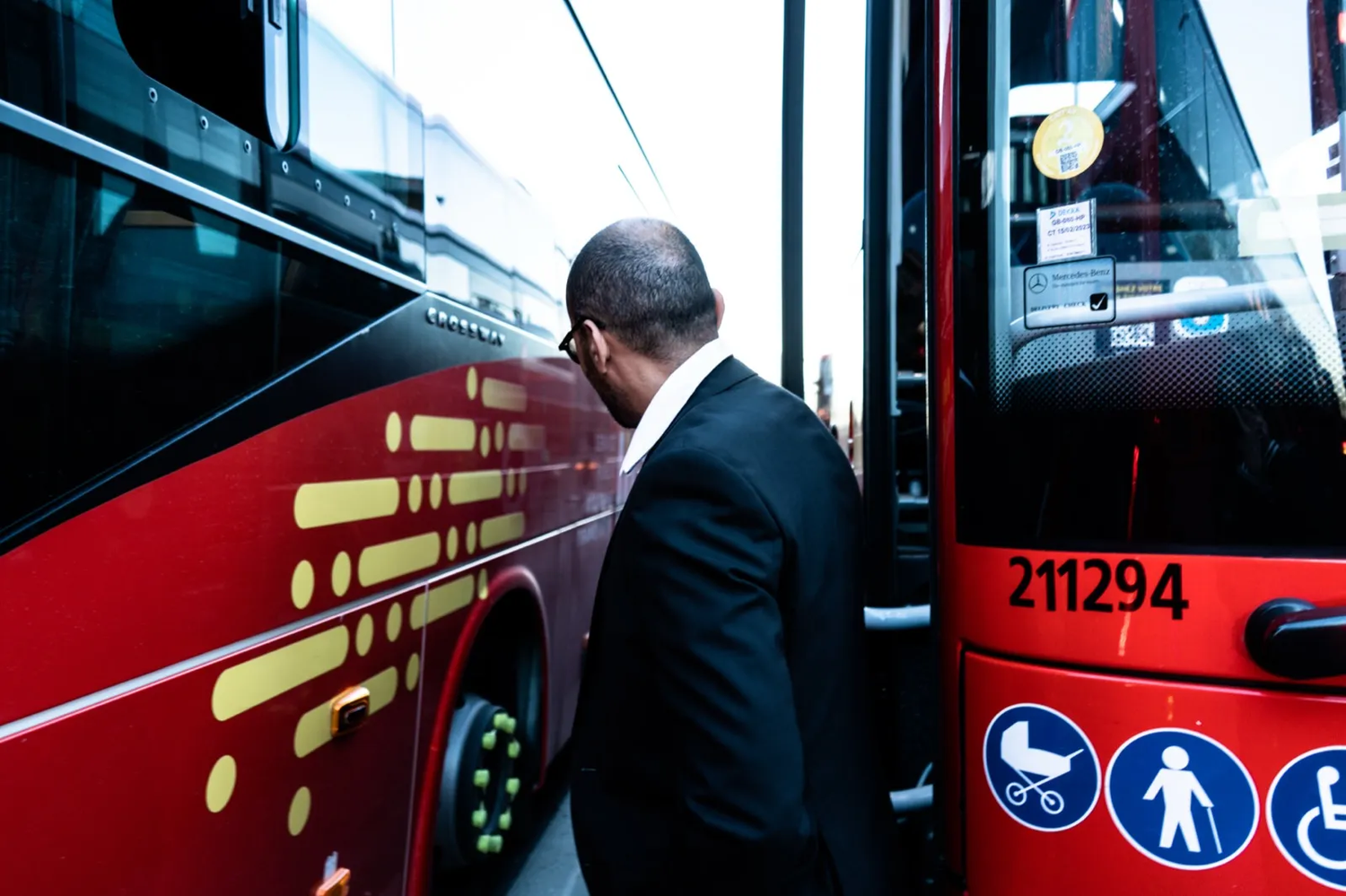 Un homme en veste noire entre dans un bus rouge estampillé Lio, dont les pictogrammes d’accessibilité sont visibles sur la porte.