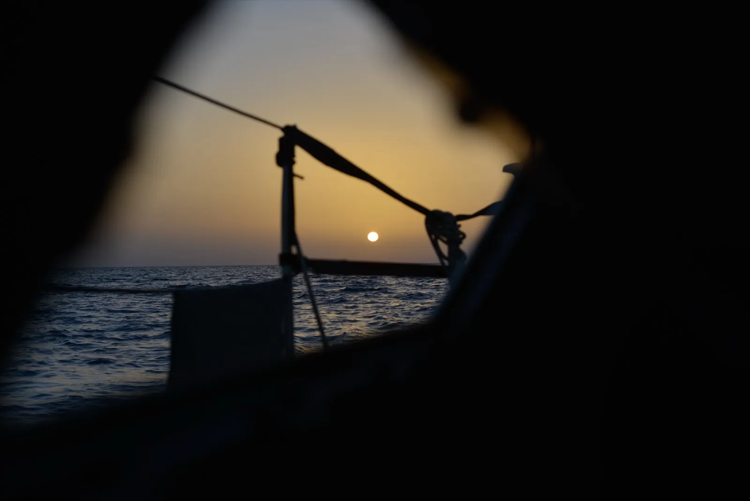 Vue du soleil couchant à travers les lignes du bateau, mer calme à l’horizon.