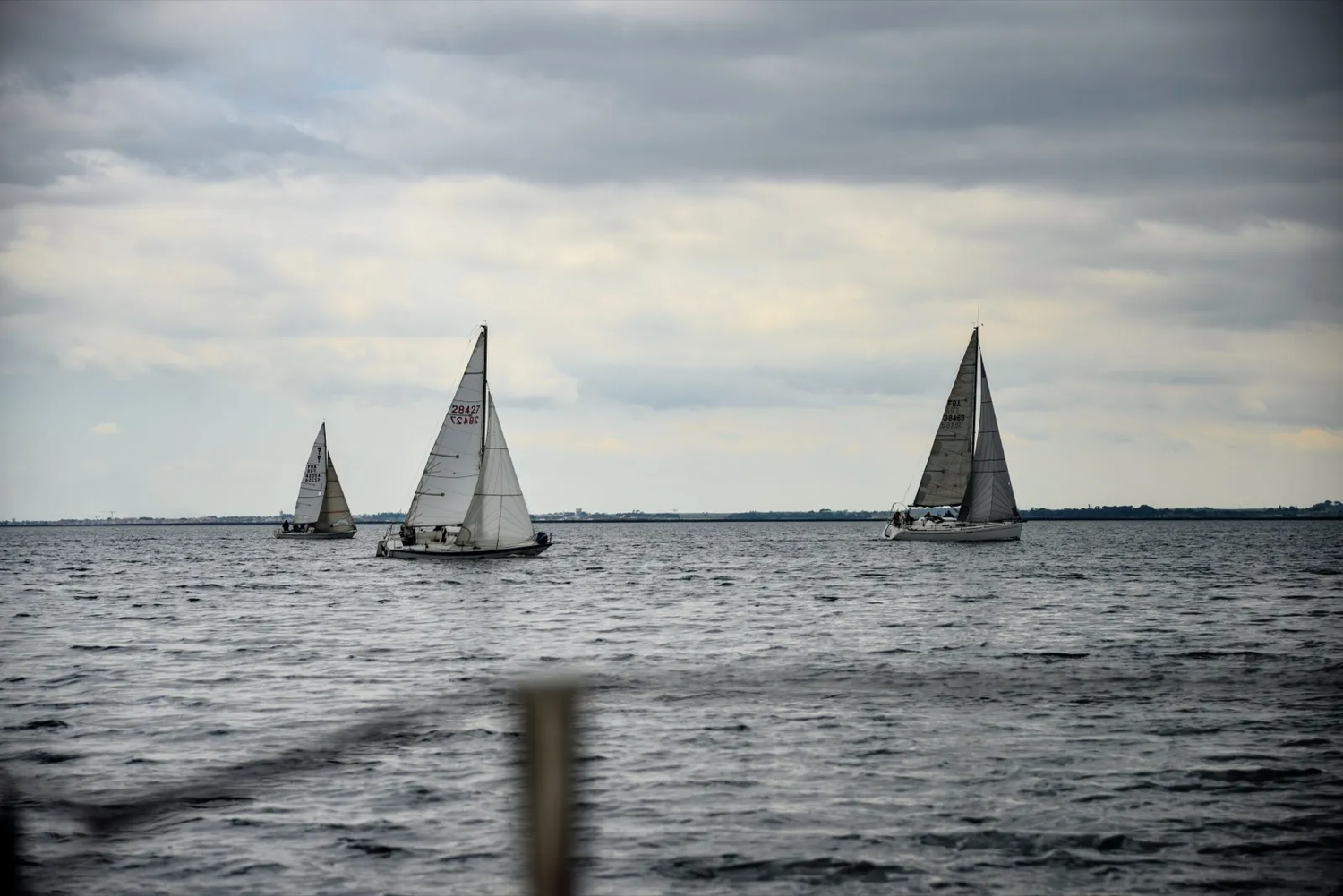 Quatre voiliers naviguant à bonne distance les uns des autres sur une mer grise, sous un ciel nuageux.