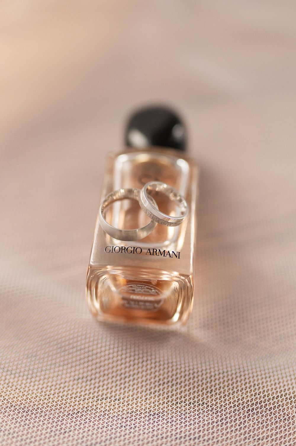 Wedding rings resting on Giorgio Armani perfume bottle on soft beige fabric background.