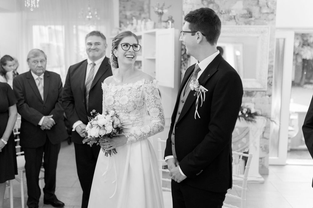 Black and white photo of bride and groom standing at altar with wedding guests seated behind.