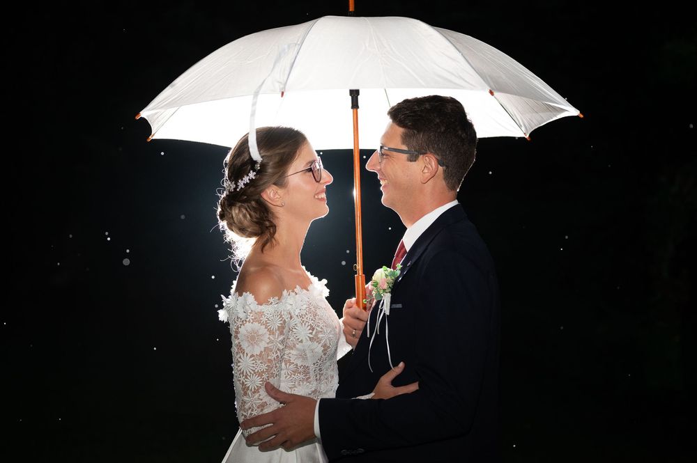 Bride and groom sharing a romantic moment under a white umbrella in the rain on their wedding night.
