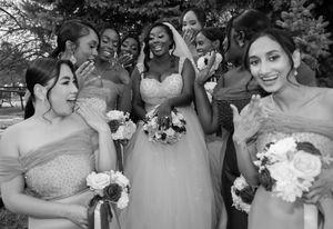A bridal party in matching dresses shares a candid laughing moment while holding bouquets during an outdoor wedding.