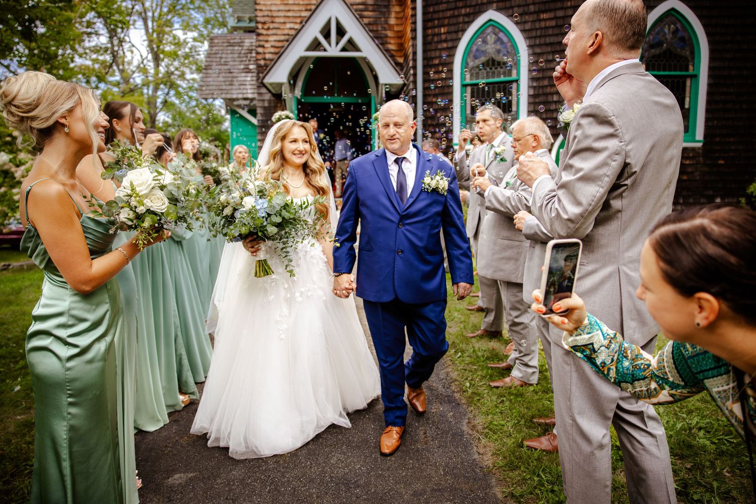 Outdoor wedding celebration with guests in sage green and gray attire gathered in a garden setting.