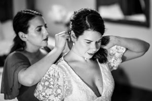 Bridesmaid helps bride put on earrings while getting ready in black and white photo.