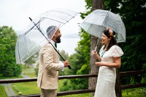 Bride and groom share a joyful moment under clear umbrellas on a rainy wedding day.