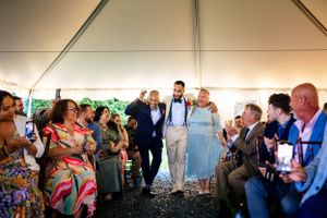 Groom makes grand entrance through cheering wedding guests under a white reception tent.