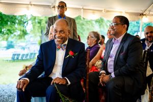 Two elegantly dressed older men smile and laugh together during an outdoor wedding ceremony.