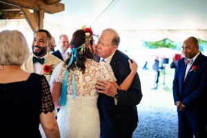 Bride hugging an older man at a colorful outdoor wedding reception under a white tent.