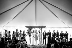 Black and white photo of a wedding ceremony under a tent with bridal party at the altar.