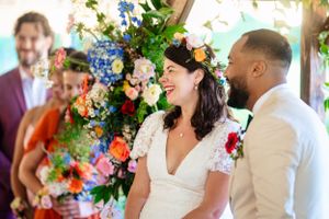 Smiling bride and groom share a joyful moment at ceremony with vibrant floral arrangement.