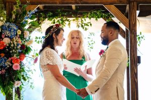 Bride and groom holding hands at altar with officiant and colorful floral arch backdrop.