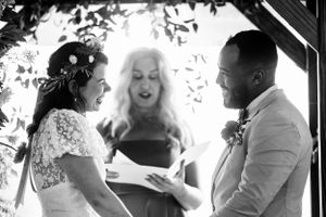 Black and white photo of bride and groom laughing with expressive officiant at wedding ceremony.