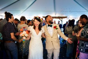Bride and groom celebrate wedding exit with confetti and cheering guests inside a tent.