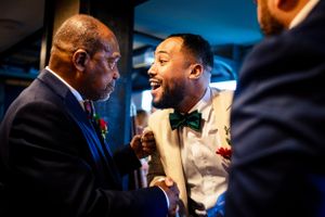 Two men share a joyful handshake and laugh together at a wedding reception celebration.