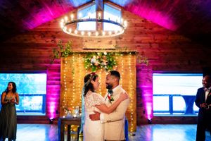Bride and groom share a romantic moment under fairy lights at rustic barn wedding.