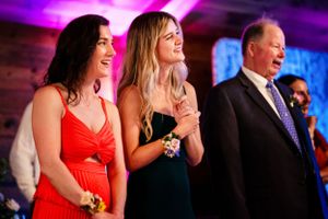 Two women in elegant dresses and an older man smile during a wedding reception.