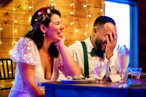 Bride and groom laugh together during wedding speeches at a rustic barn reception.
