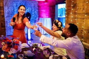 Bridesmaid in red dress gives a toast as bride and groom raise glasses at reception.