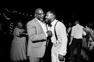 Black and white photo of two men laughing and celebrating at wedding reception.