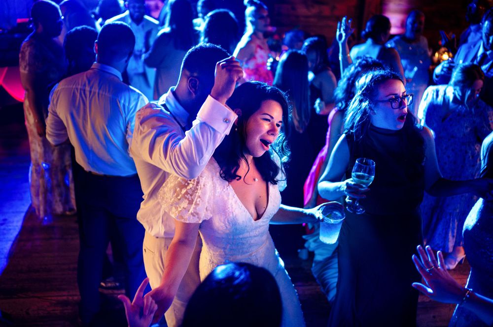 Bride dancing joyfully with guests under colorful lights at lively wedding reception.