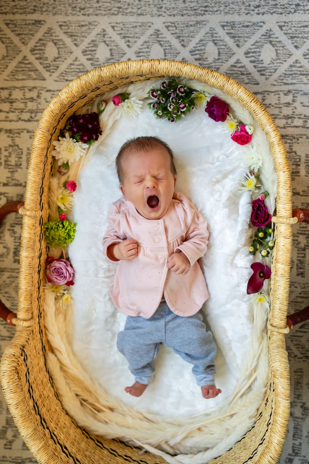 newborn girl yawns while lying in the basket with flowers