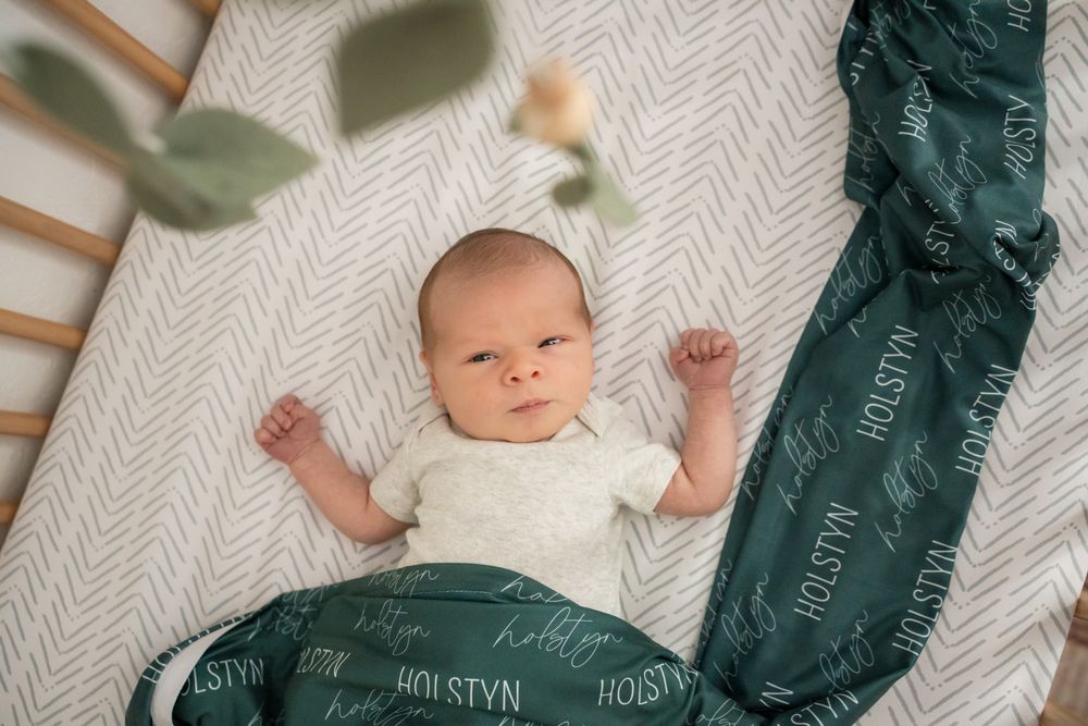 newborn baby boy portrait lying in crib with name blanket and baby mobile