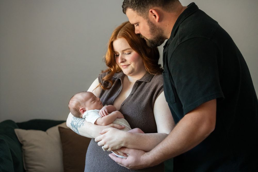 Newborn family portraits in the family's home as Mom holds newborn son while dad looks at baby