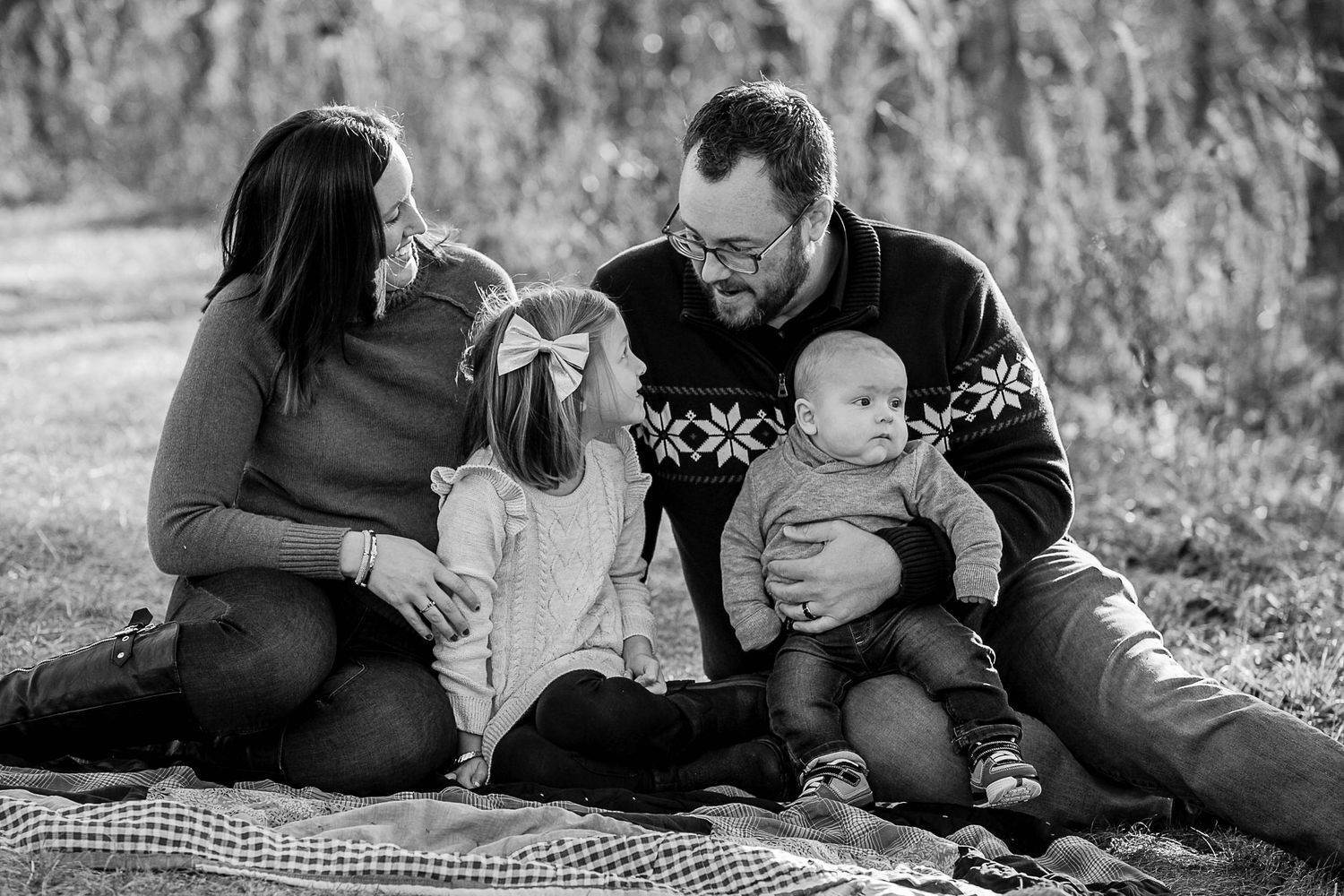 Family members lying on a checkered blanket sharing intimate moments outdoors.