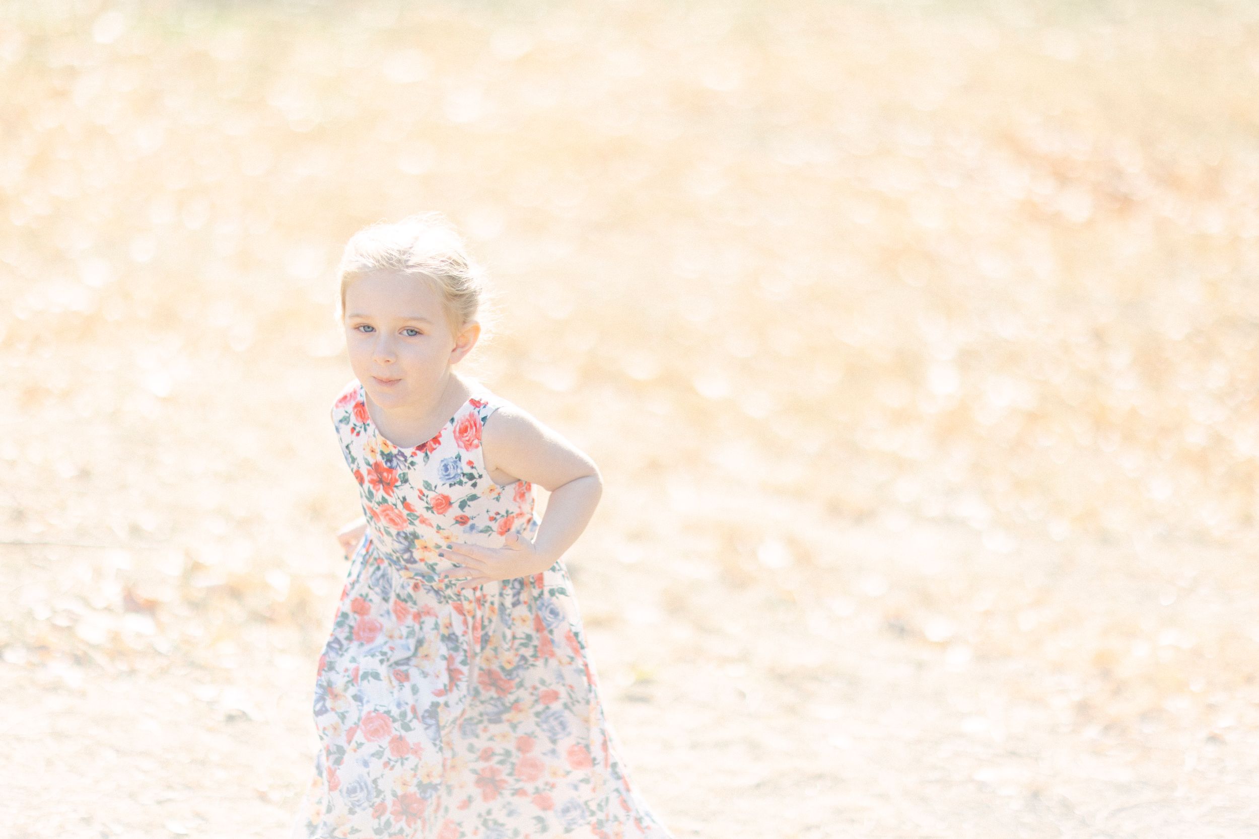 A child in a floral dress plays in a sun-drenched field with golden light.