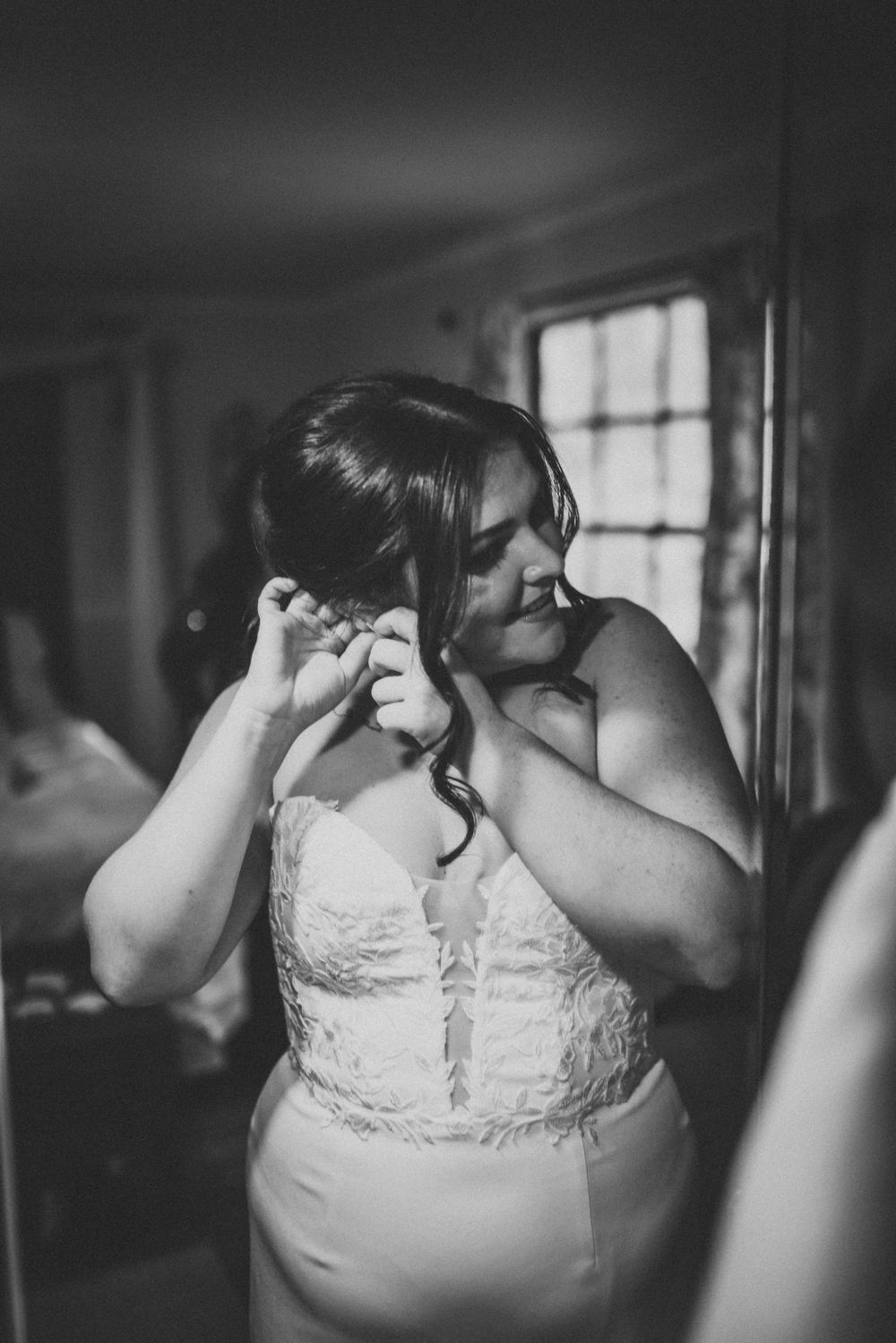 Black and white portrait of someone putting on earrings while wearing elegant white dress.