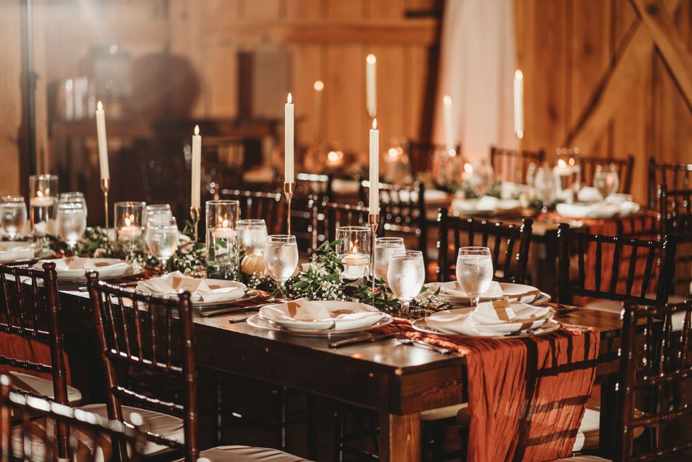 Elegant wedding reception table setting with candles and place settings in a rustic wooden barn venue.