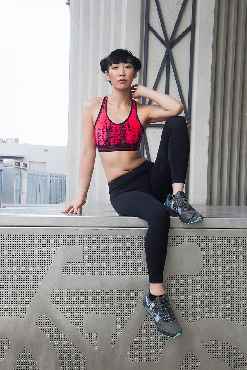 Athletic figure in red sports bra and black leggings poses on urban architecture.