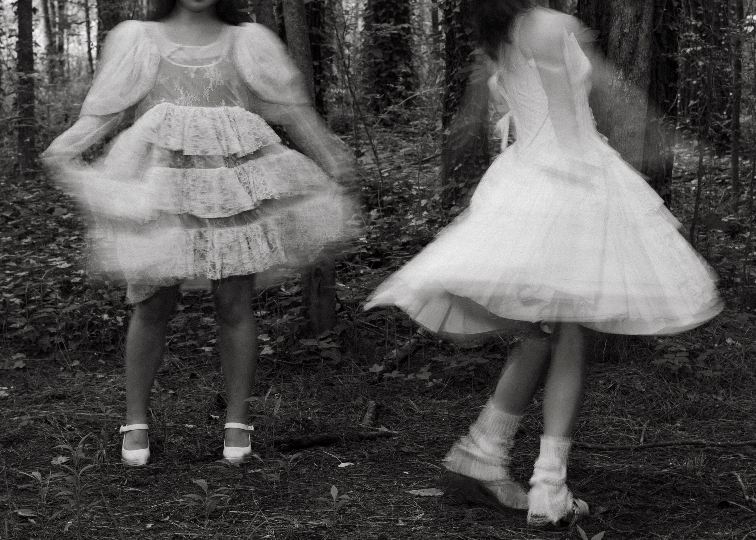 Two models wearing white dresses in a forest