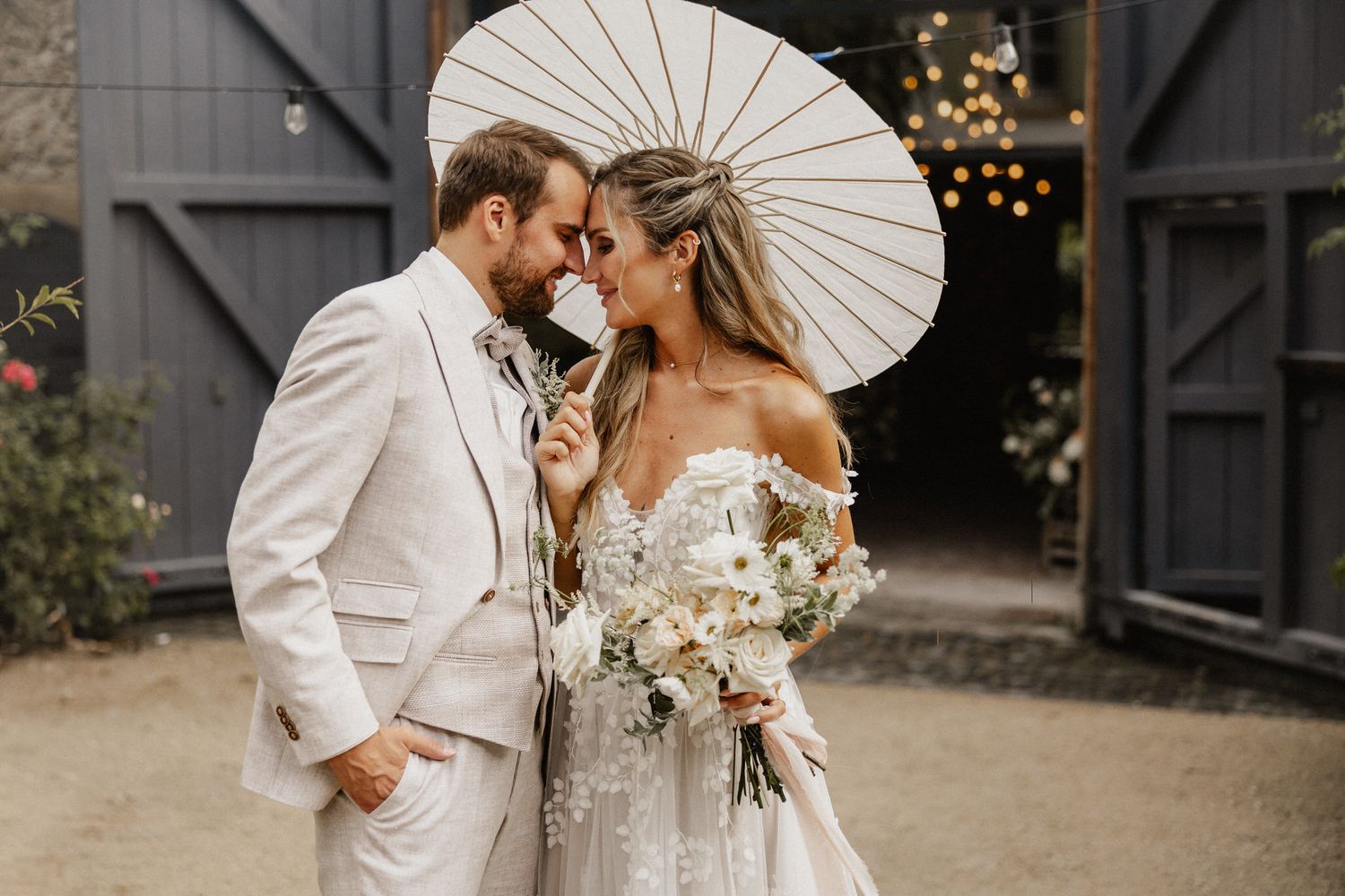 Romantic wedding photos with white parasol and rustic barn setting.