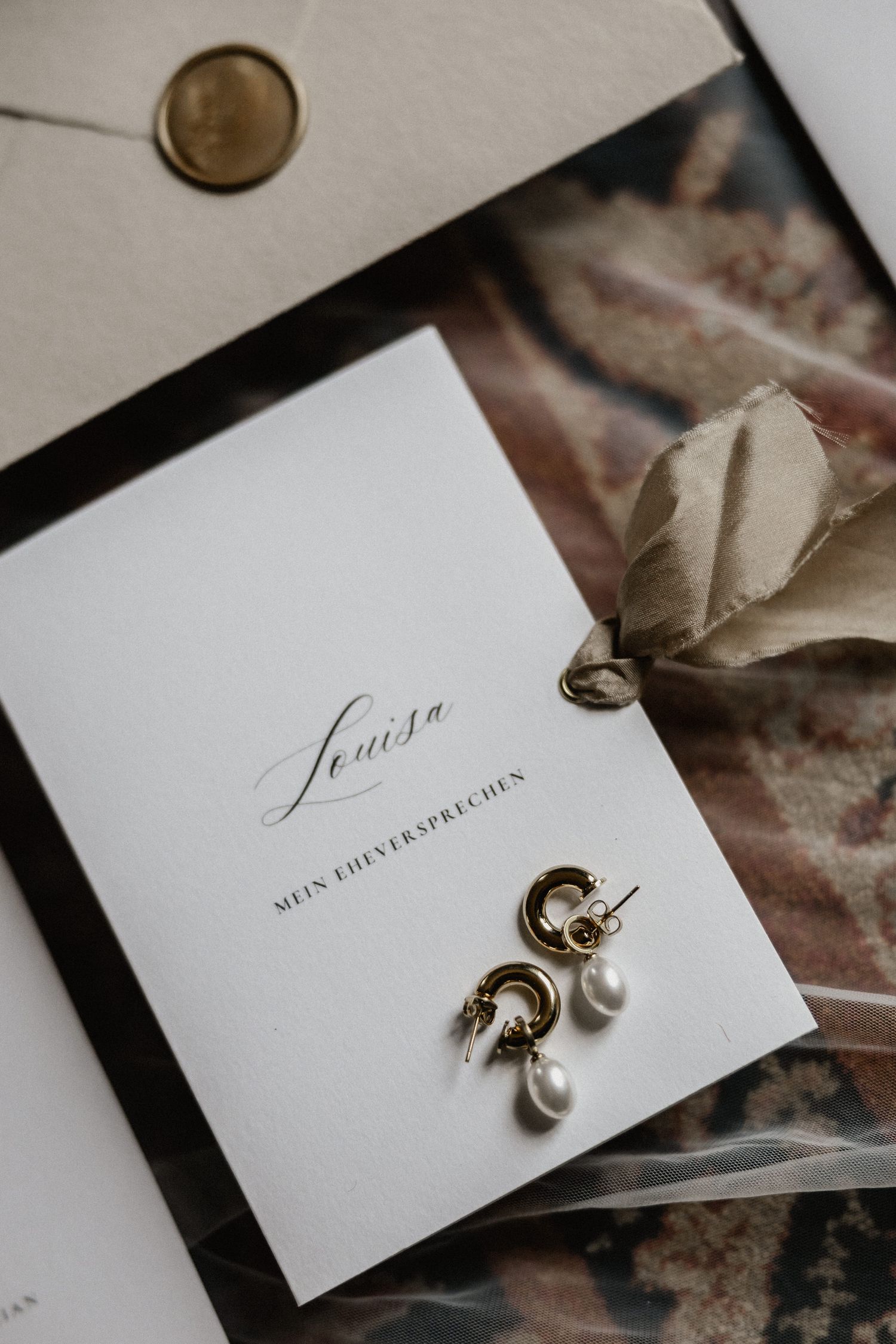 Wedding place cards with elegant script lettering displayed with pearl drop earrings.