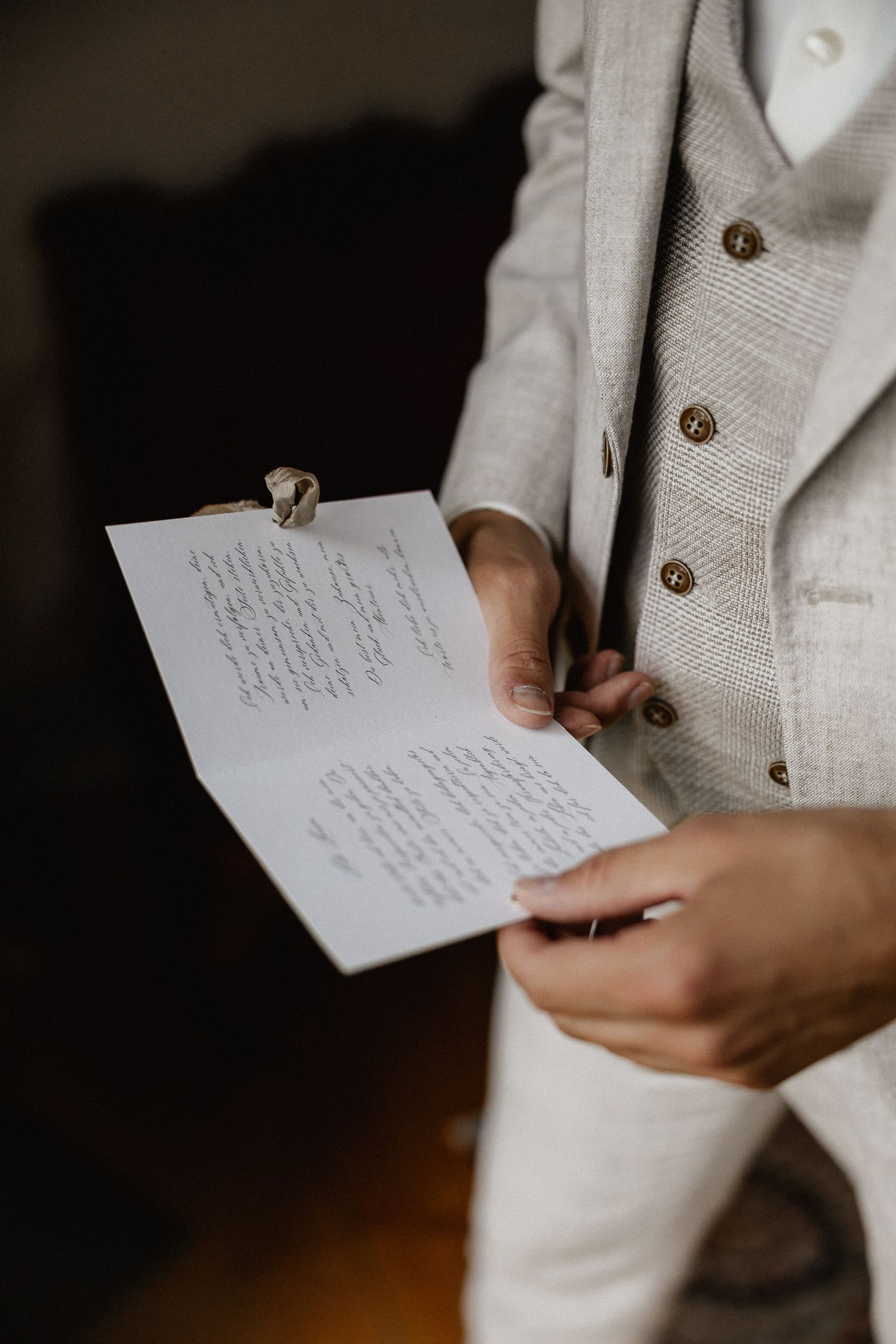 Close-up of hands holding handwritten wedding vows on white paper against dark background.