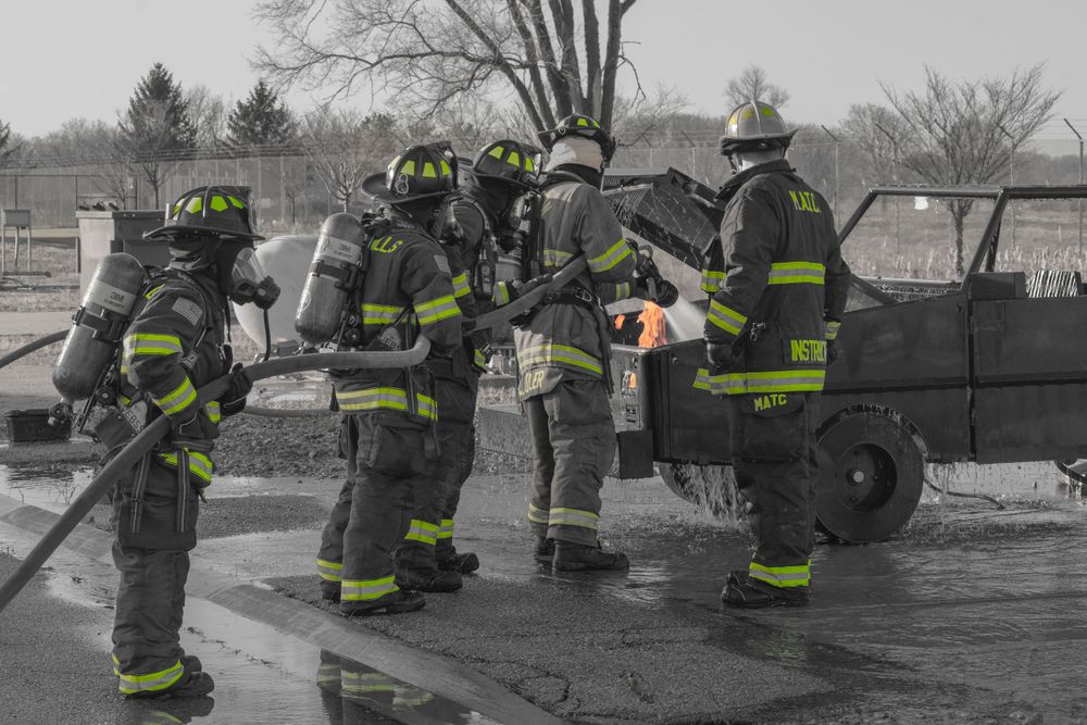 Firefighters in protective gear working around vehicle in black and white photo.