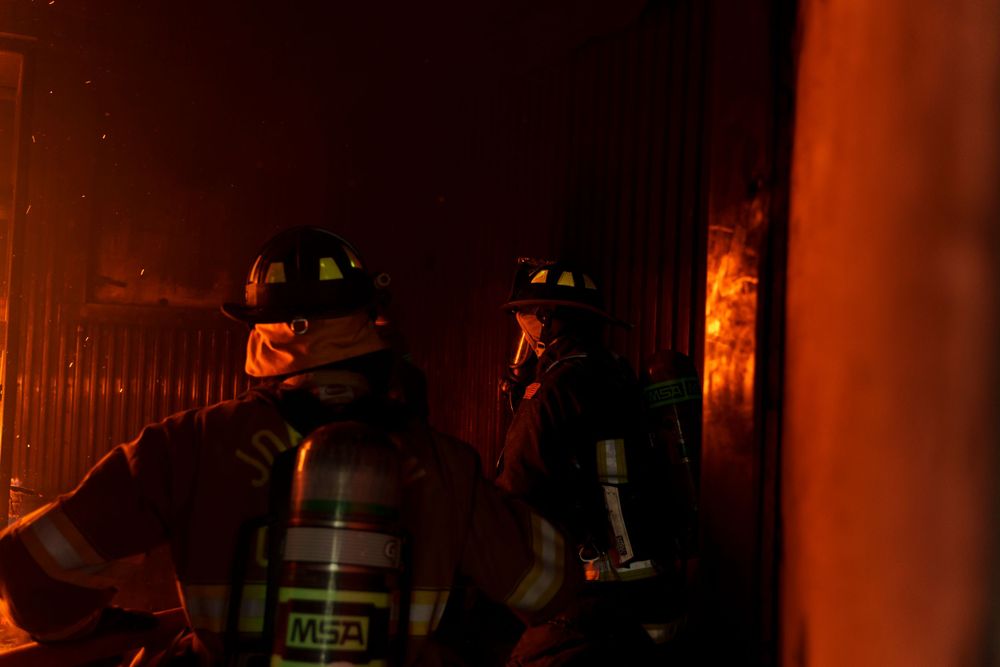 Firefighters battle intense flames inside a burning building at night.