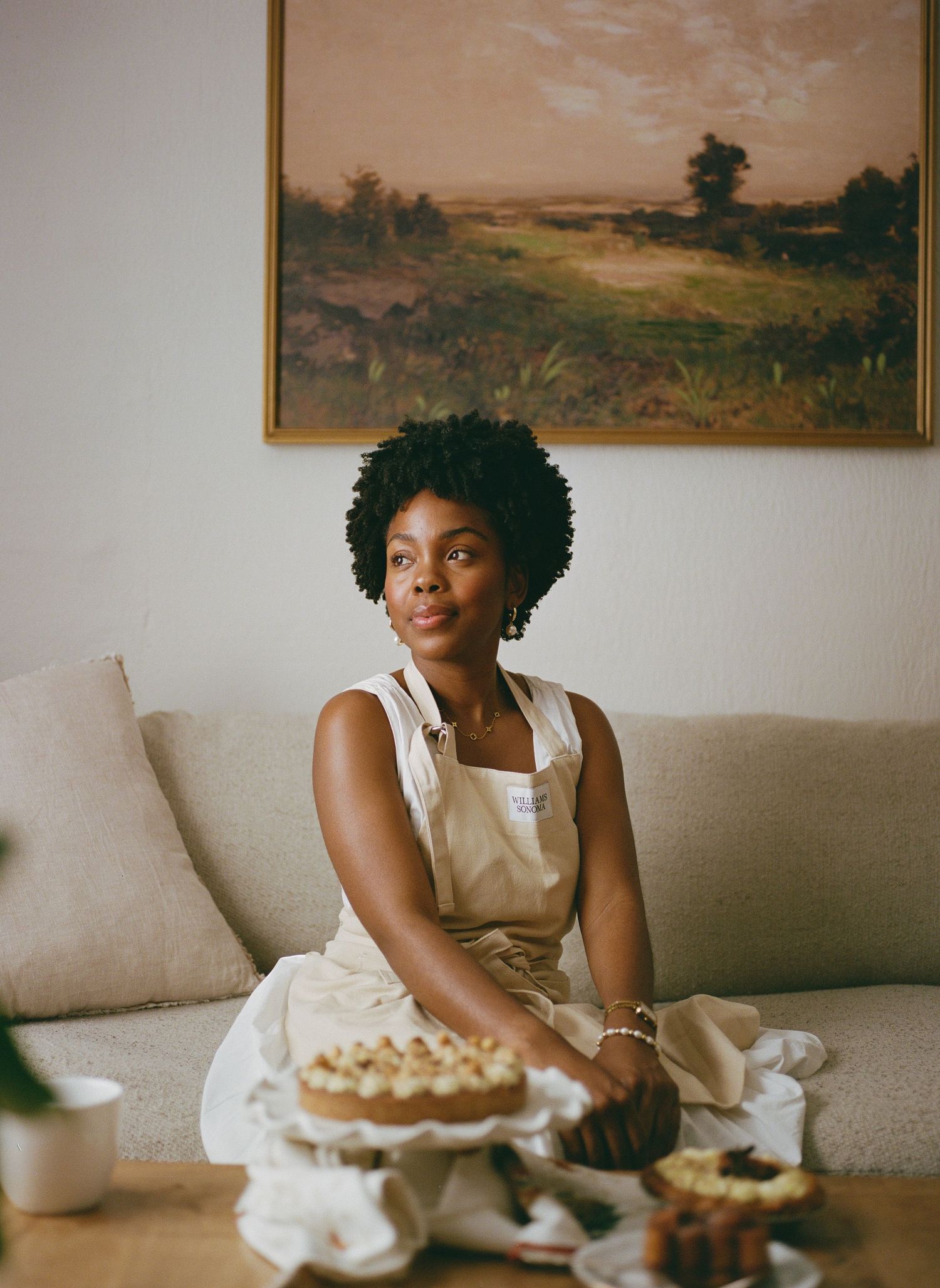 Person enjoying pie and coffee while relaxing on beige couch with landscape artwork in background.