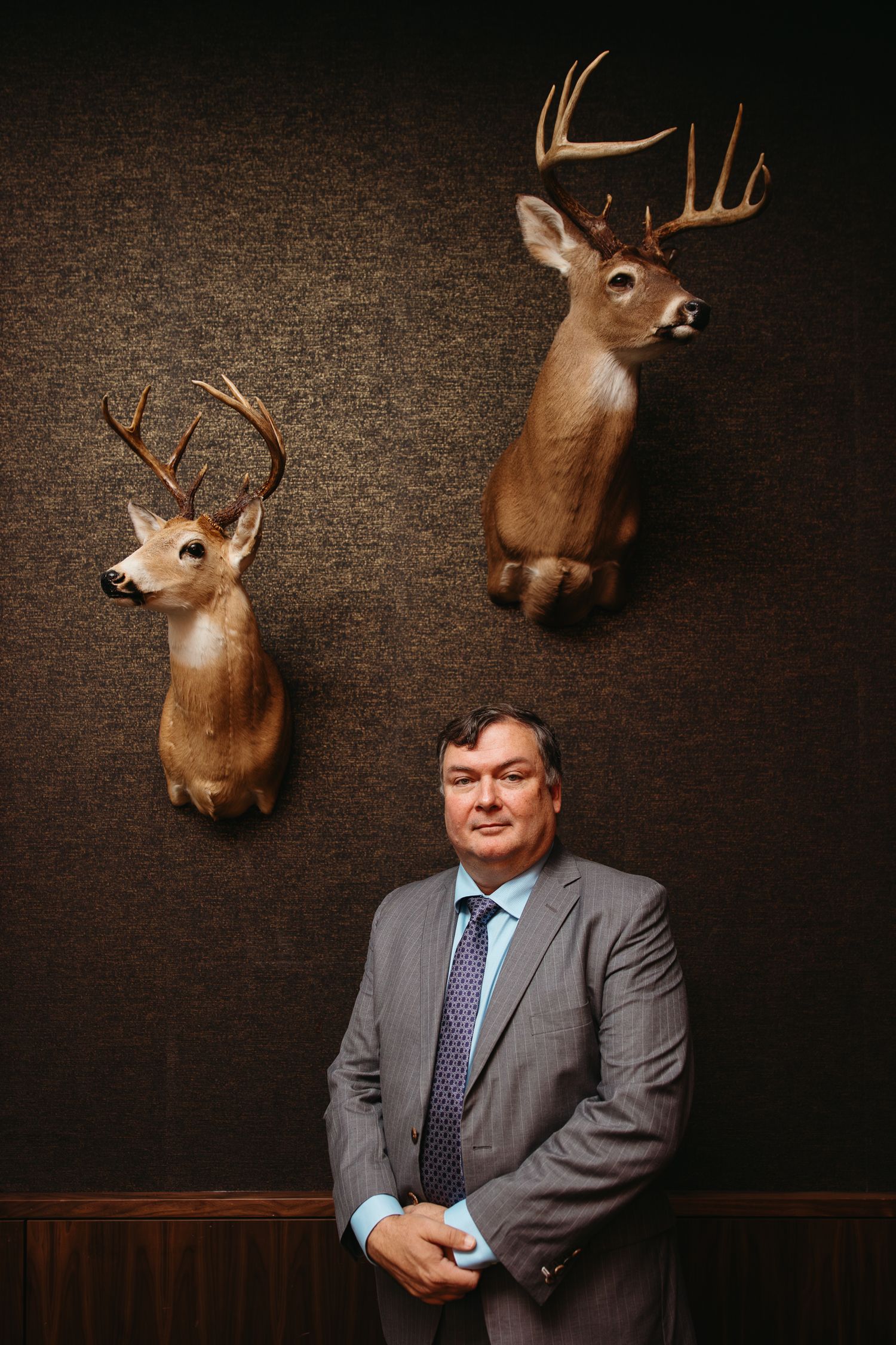 Business portrait with mounted deer heads on dark textured wall.