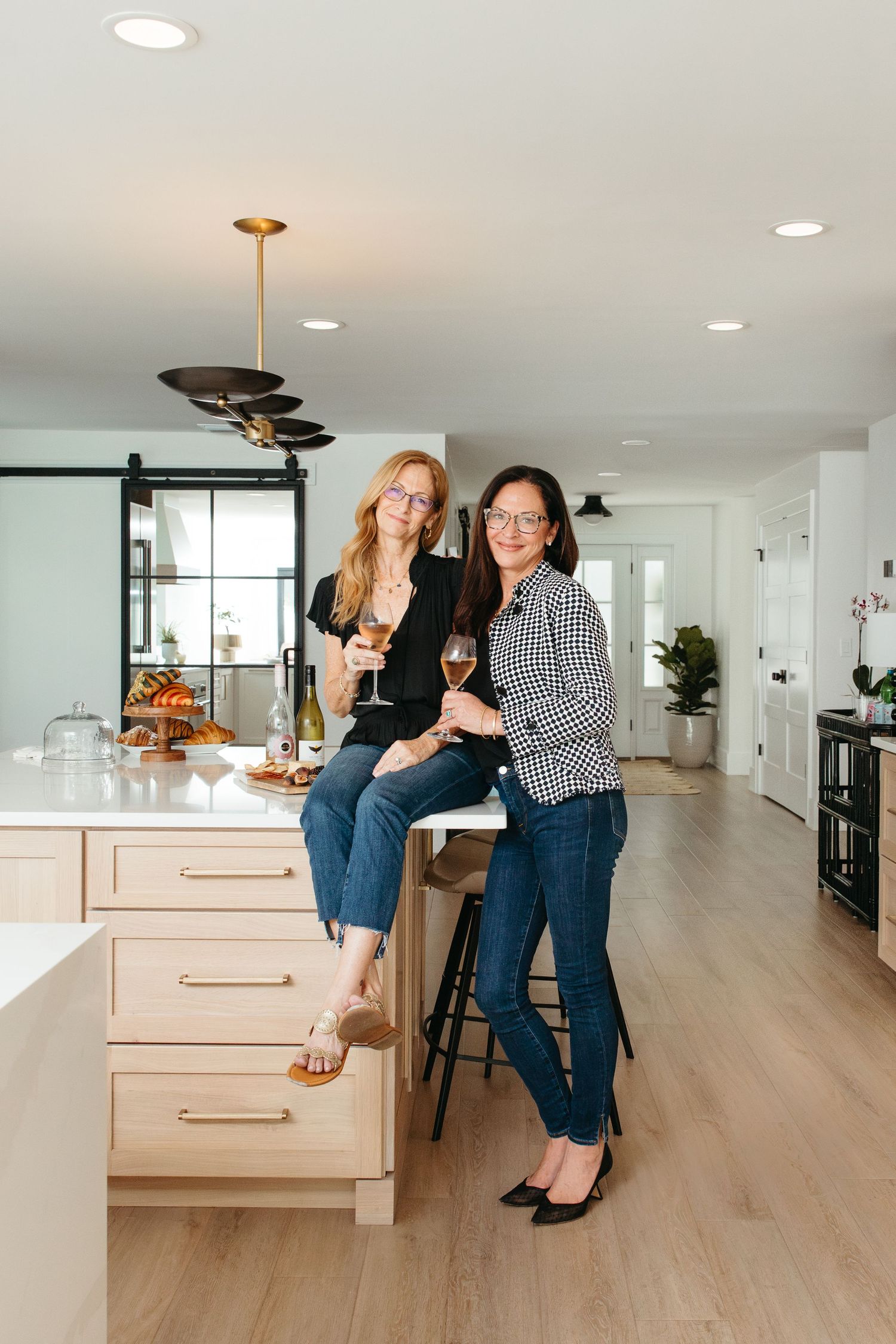 Couple poses together in modern kitchen with light wood floors and white cabinetry.