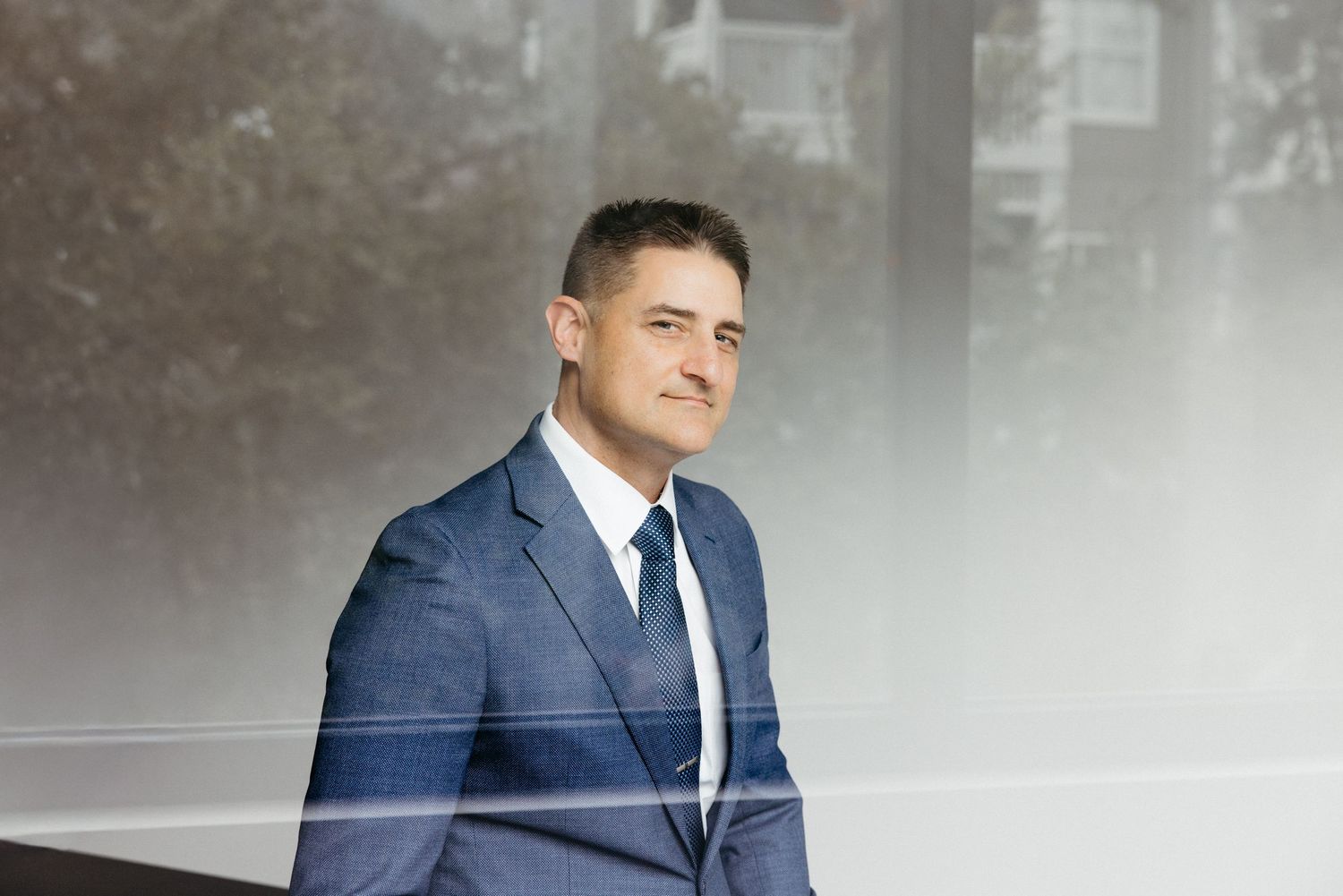 Professional businessman in blue suit and tie posing confidently outdoors in a modern corporate setting.