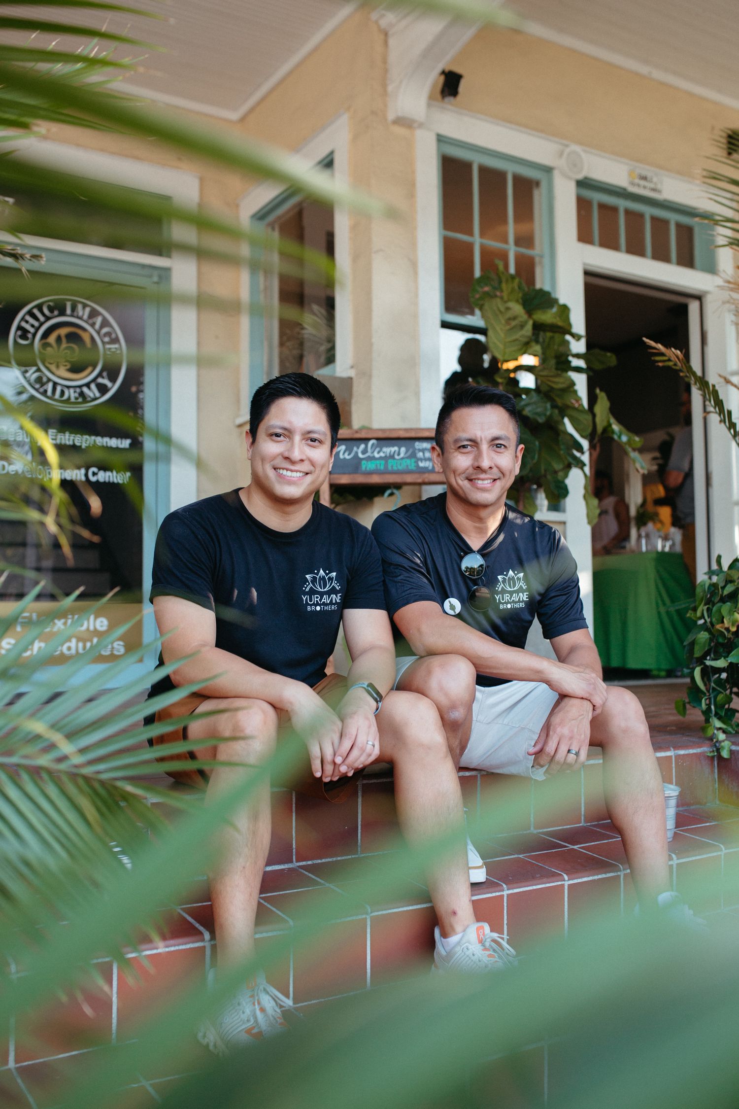Staff members in black uniforms sitting on outdoor steps with palm fronds in foreground.
