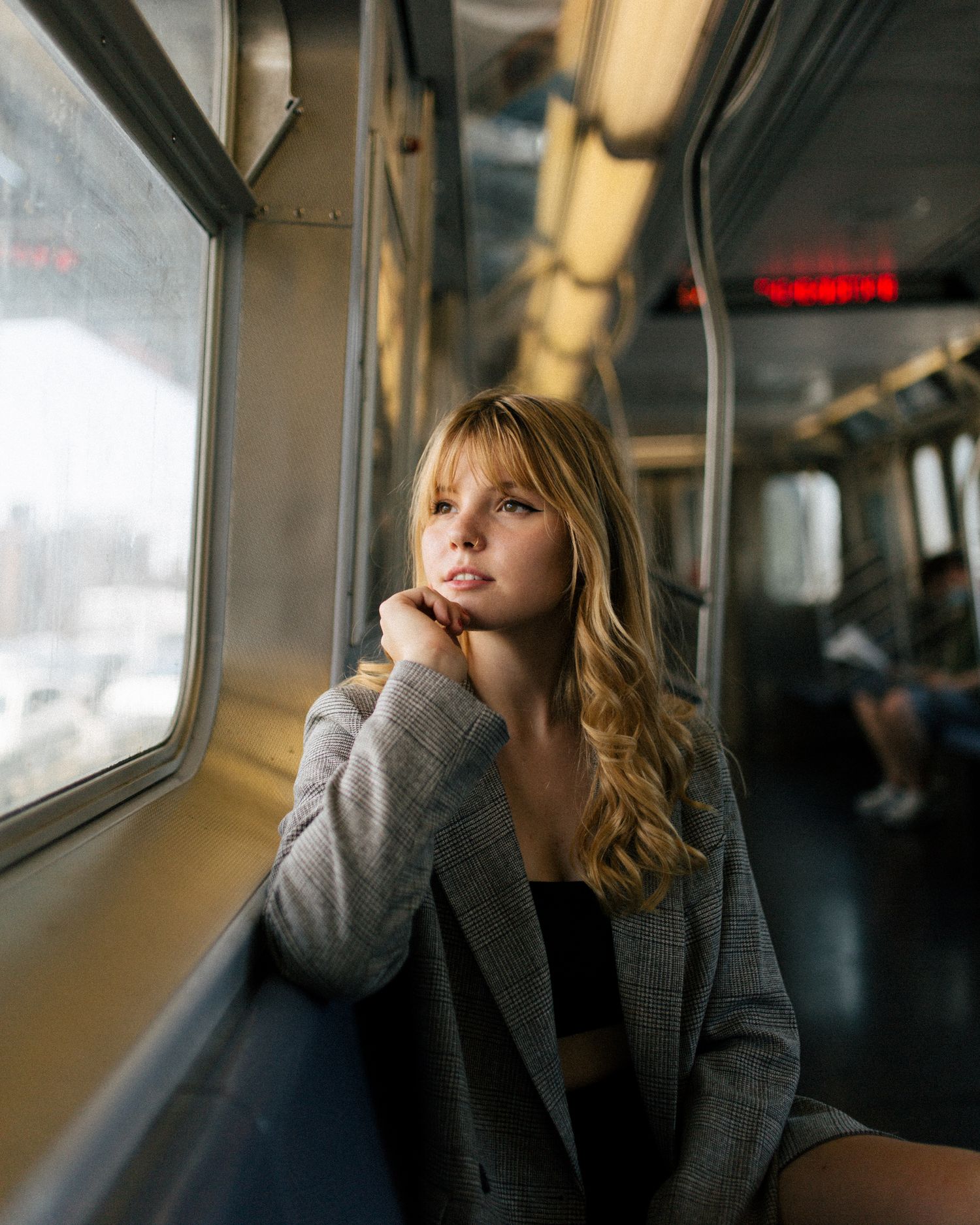 Person gazing thoughtfully out train window wearing grey blazer during commute.