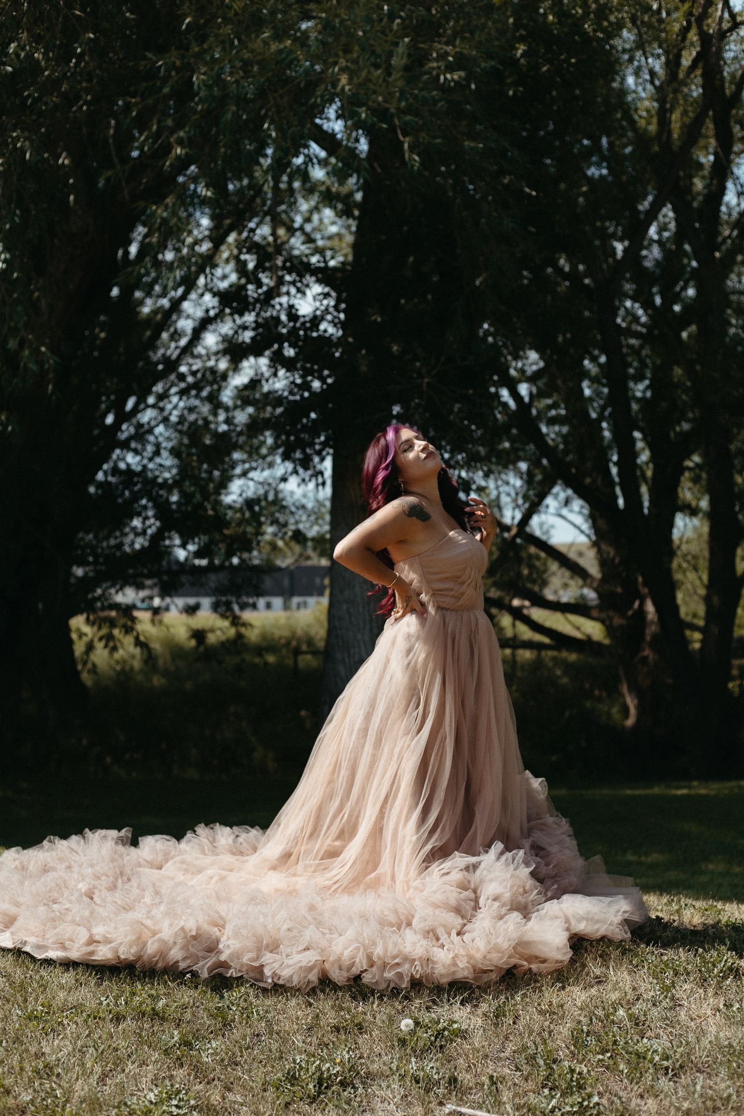 Artistic outdoor photography of a flowing pink ballgown on grass beneath trees.