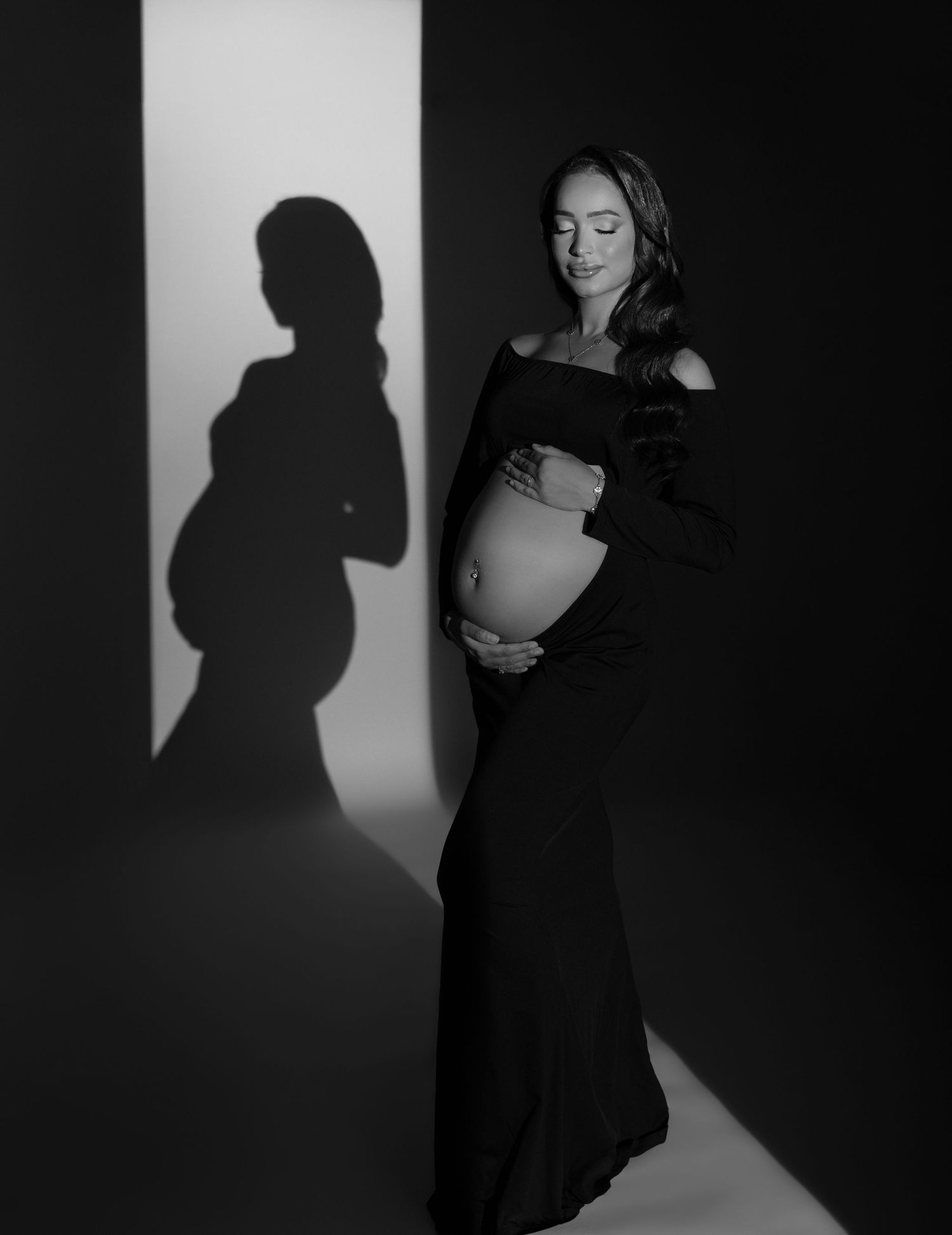 Maternity photo of woman in brown silk wrap holding white flowers against dark background.